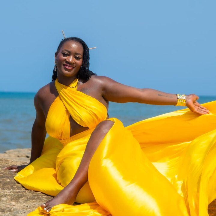 Loreta Waziri, founder of Pathways to Joyful Living, smiling in a flowing yellow gown by the sea